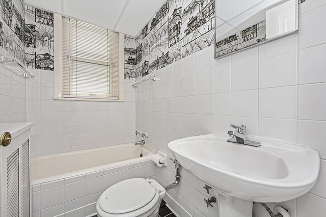 bathroom with tile walls, toilet, a sink, and bathing tub / shower combination