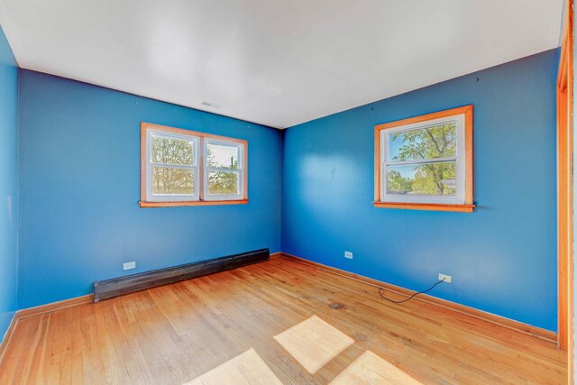 unfurnished room featuring a baseboard radiator, plenty of natural light, and wood finished floors
