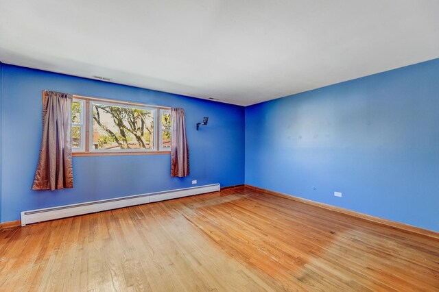 empty room featuring a baseboard heating unit, baseboards, and wood finished floors