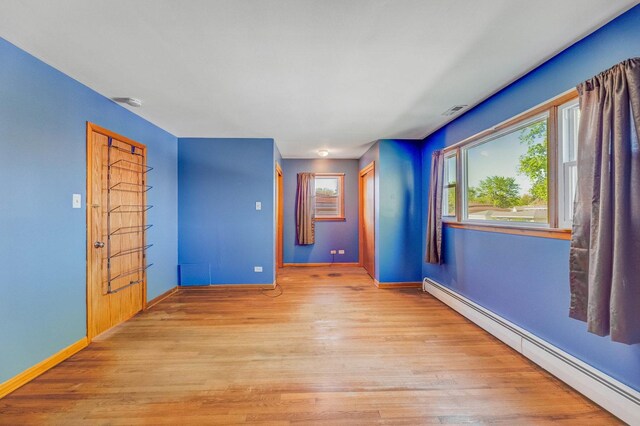 unfurnished room featuring baseboard heating, light wood-style flooring, and baseboards