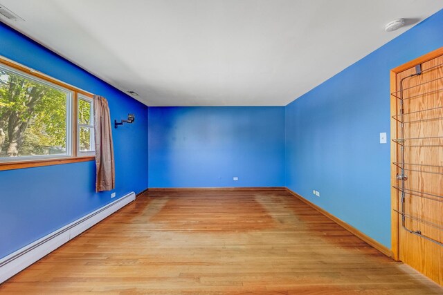 empty room featuring baseboard heating, wood finished floors, a smoke detector, and baseboards