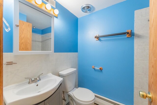 bathroom with toilet, vanity, a baseboard heating unit, and tile walls