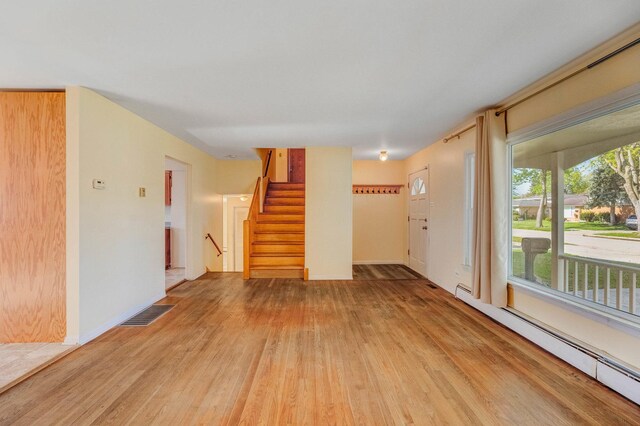 unfurnished living room featuring a baseboard heating unit, light wood finished floors, and stairs