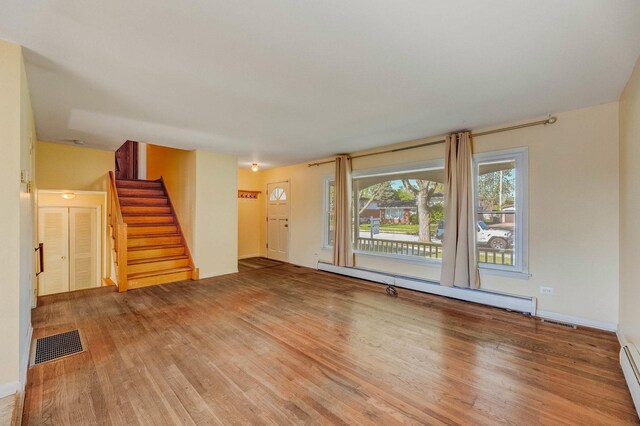 unfurnished living room with baseboard heating, stairs, wood finished floors, and baseboards