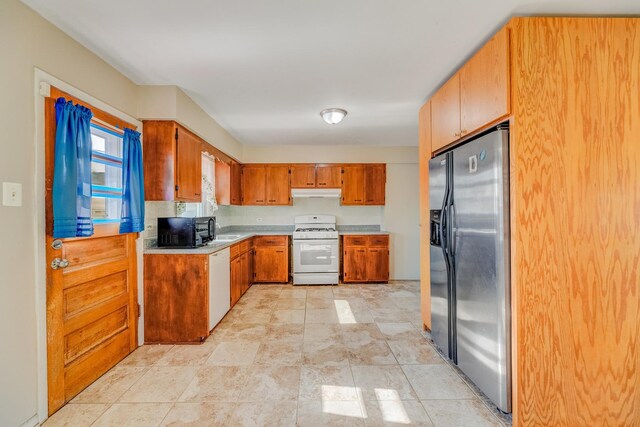 kitchen featuring white appliances, under cabinet range hood, light countertops, a sink, and brown cabinets