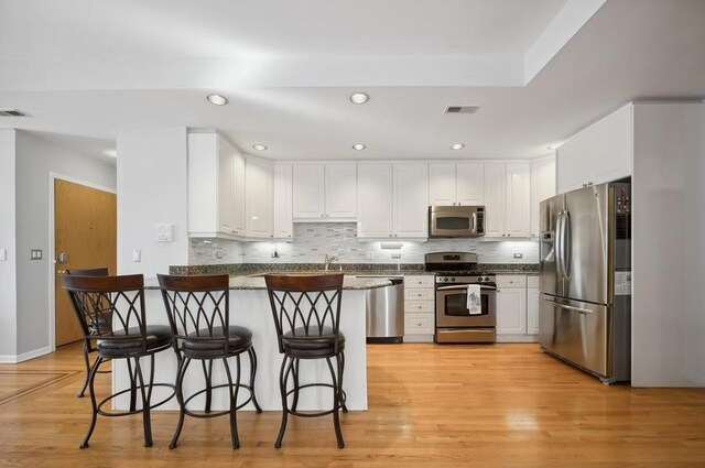 kitchen with stainless steel appliances, a peninsula, dark countertops, white cabinetry, and decorative backsplash