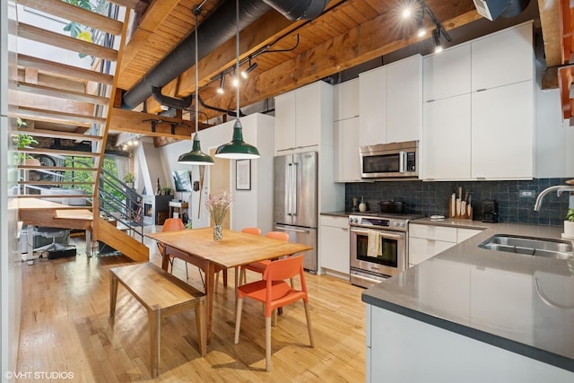 kitchen with appliances with stainless steel finishes, a sink, light wood-type flooring, backsplash, and white cabinetry