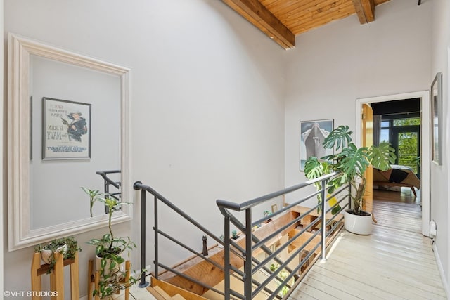 hall with an upstairs landing, wood finished floors, beamed ceiling, and wood ceiling