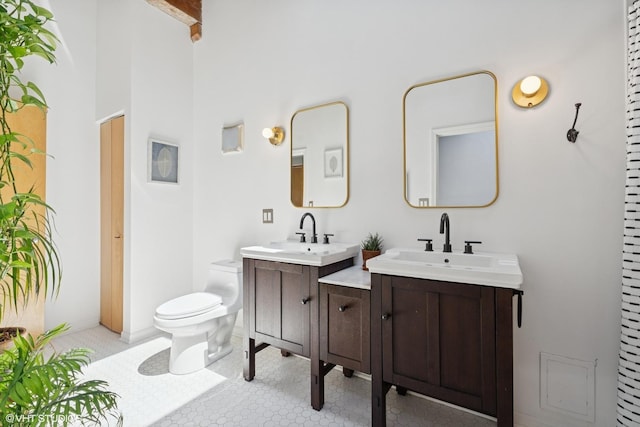 bathroom with toilet, two vanities, beamed ceiling, and a high ceiling
