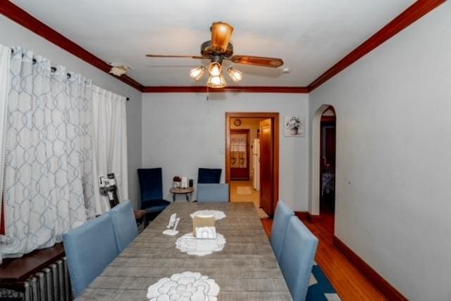 dining room with a ceiling fan, crown molding, arched walkways, wood finished floors, and radiator heating unit