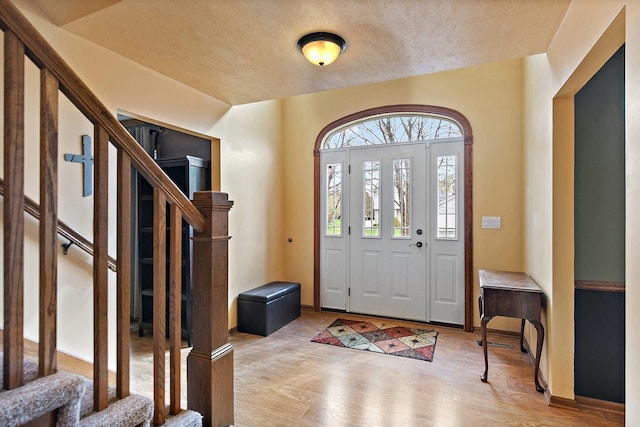 foyer featuring a textured ceiling, baseboards, light wood finished floors, and stairs