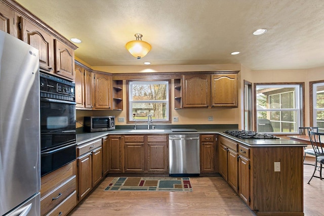 kitchen featuring a sink, open shelves, a warming drawer, a peninsula, and appliances with stainless steel finishes