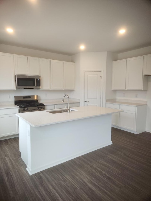 kitchen with white cabinetry, a sink, stainless steel appliances, dark wood-type flooring, and an island with sink