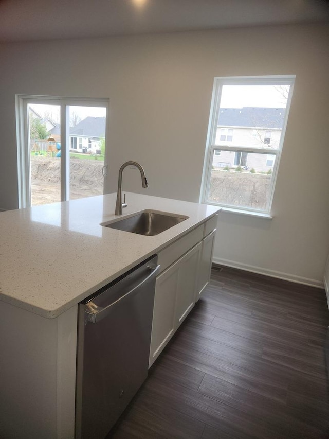kitchen with stainless steel dishwasher, a sink, dark wood-style flooring, light stone countertops, and an island with sink