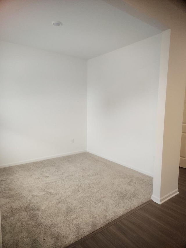spare room featuring dark wood finished floors, dark colored carpet, and baseboards