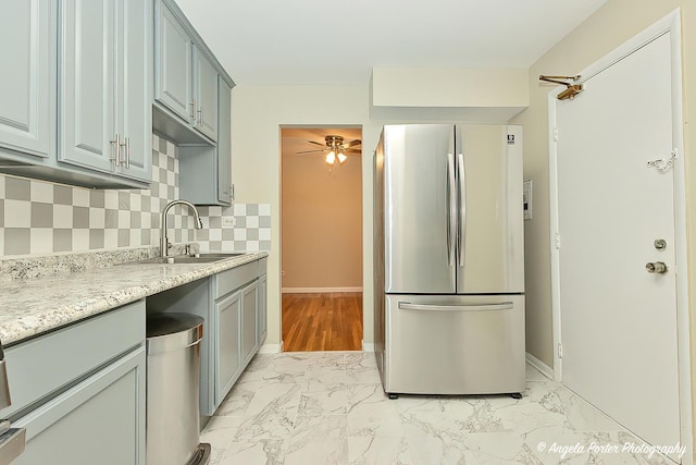 kitchen featuring a sink, marble finish floor, freestanding refrigerator, a ceiling fan, and decorative backsplash