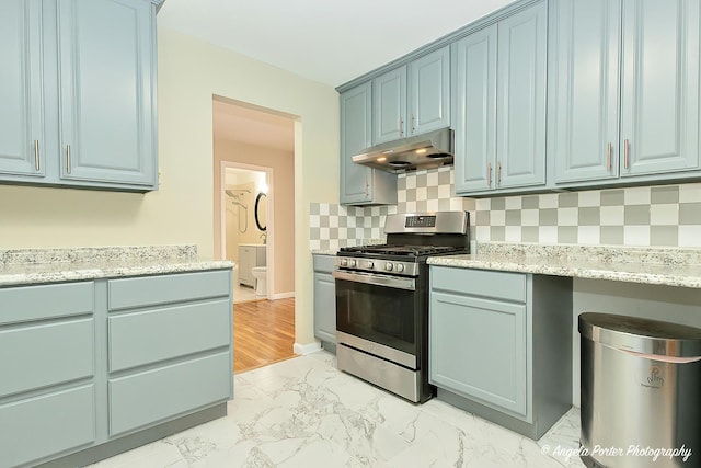 kitchen with marble finish floor, under cabinet range hood, backsplash, gas stove, and blue cabinetry
