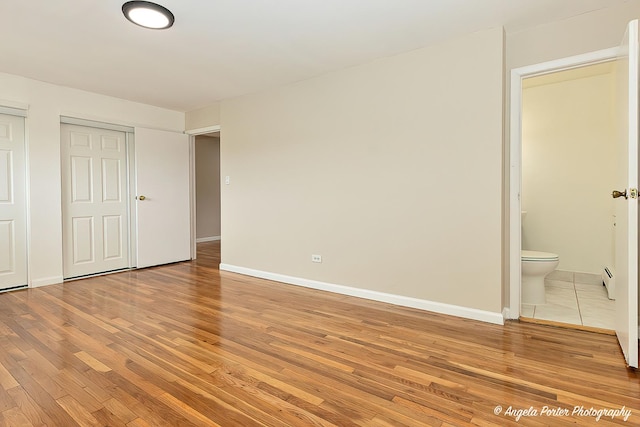 unfurnished bedroom with baseboards, ensuite bathroom, and light wood-style floors