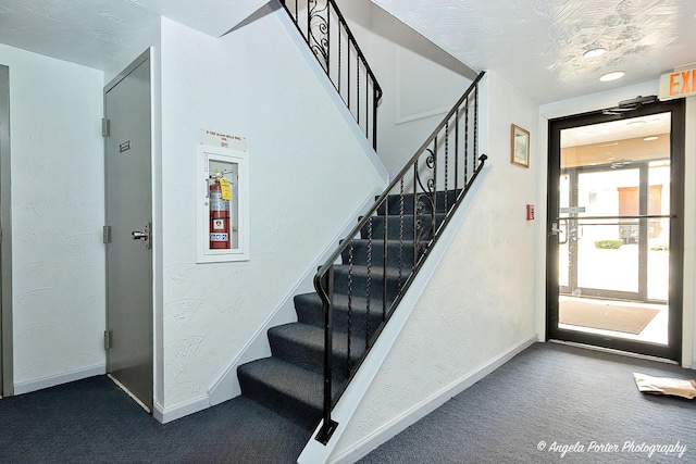 staircase featuring baseboards, a textured wall, and carpet