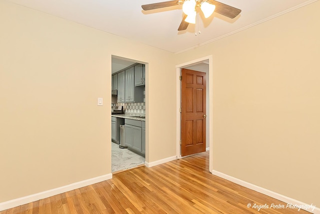 spare room with crown molding, ceiling fan, baseboards, and light wood-style floors