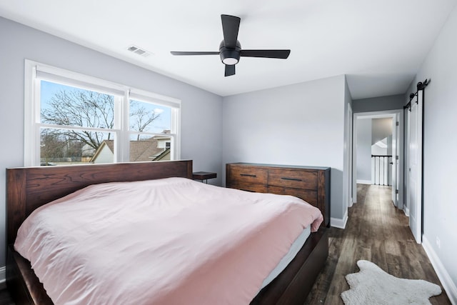 bedroom featuring a barn door, a ceiling fan, baseboards, dark wood-type flooring, and visible vents