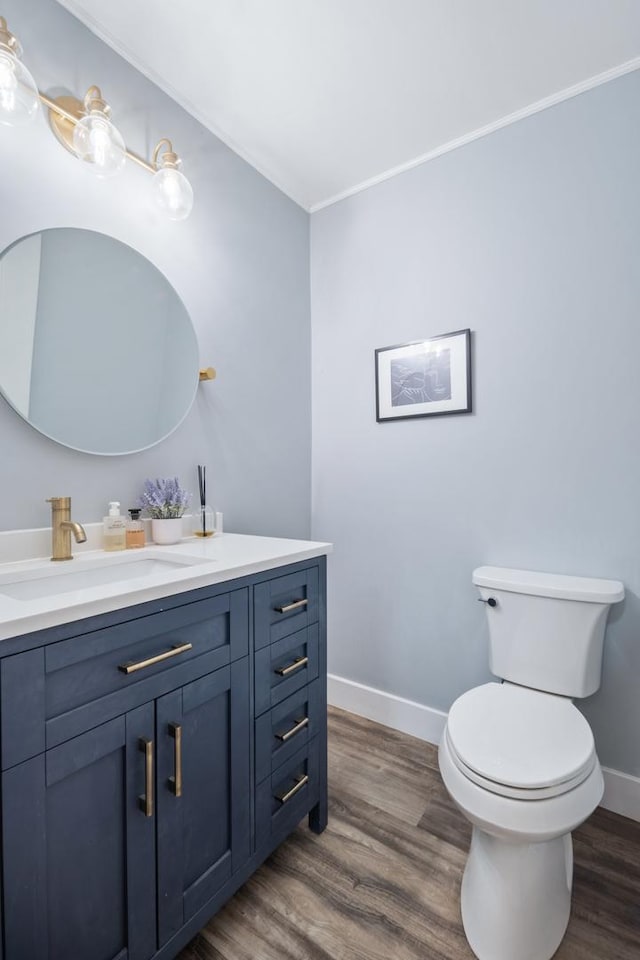 bathroom featuring wood finished floors, toilet, vanity, crown molding, and baseboards