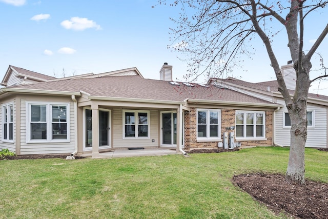 rear view of house with brick siding, a patio area, a chimney, a yard, and roof with shingles