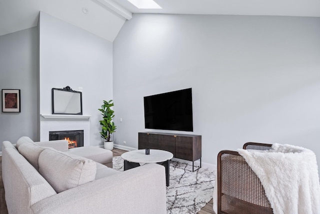living room featuring baseboards, wood finished floors, a lit fireplace, and vaulted ceiling with skylight