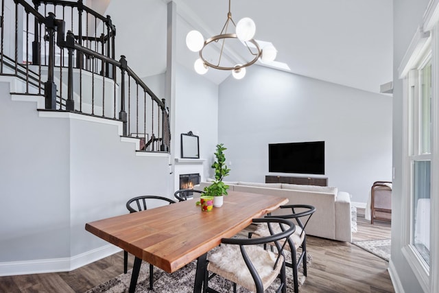 dining space featuring baseboards, an inviting chandelier, wood finished floors, stairway, and high vaulted ceiling