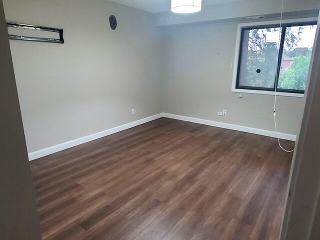 unfurnished room with baseboards and dark wood-style floors