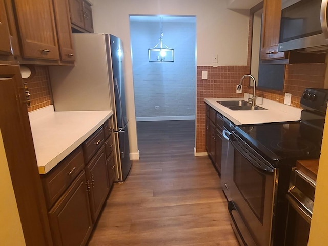 kitchen with wood finished floors, a sink, light countertops, baseboards, and stainless steel appliances