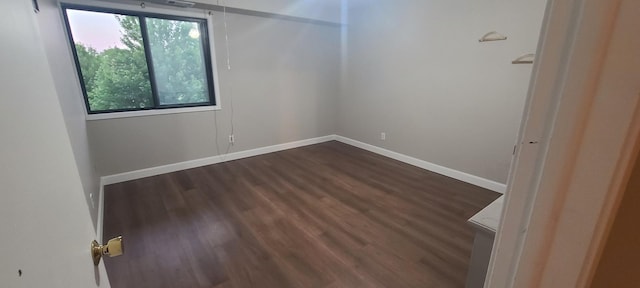 unfurnished room with baseboards and dark wood-type flooring
