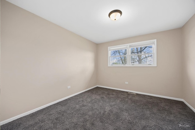 spare room featuring dark carpet, visible vents, and baseboards