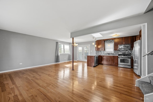 kitchen with decorative backsplash, light wood-style flooring, stainless steel appliances, light countertops, and open floor plan