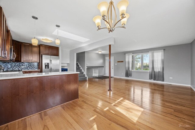 kitchen featuring light wood finished floors, decorative light fixtures, stainless steel refrigerator with ice dispenser, light countertops, and open floor plan