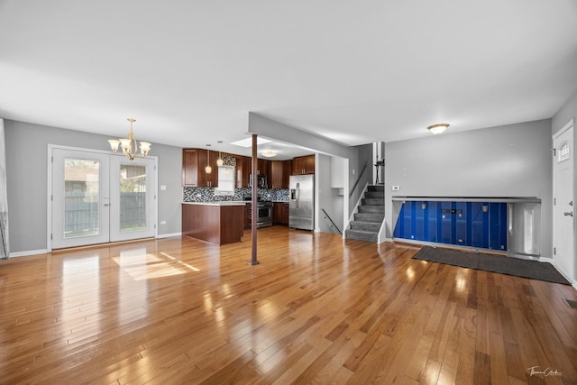 unfurnished living room with baseboards, light wood-type flooring, a notable chandelier, and stairs