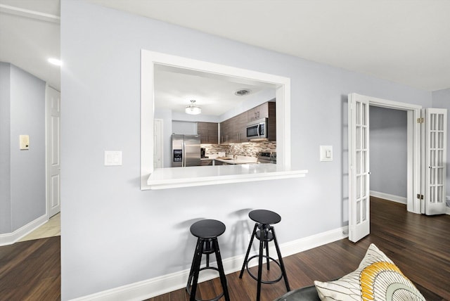kitchen featuring decorative backsplash, a kitchen bar, light countertops, appliances with stainless steel finishes, and dark wood finished floors