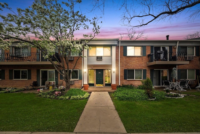 view of front of house with brick siding, a balcony, a yard, and a patio area