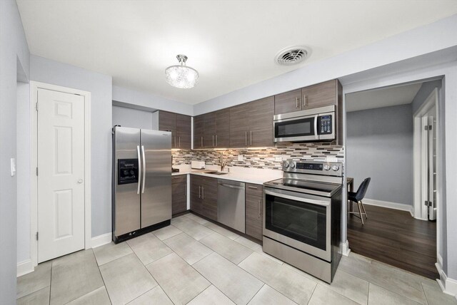 kitchen featuring dark brown cabinets, appliances with stainless steel finishes, light countertops, and decorative backsplash