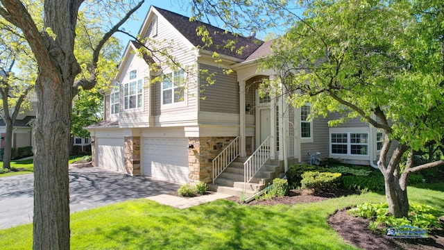 view of front of home with stone siding, a garage, driveway, a front lawn, and roof with shingles