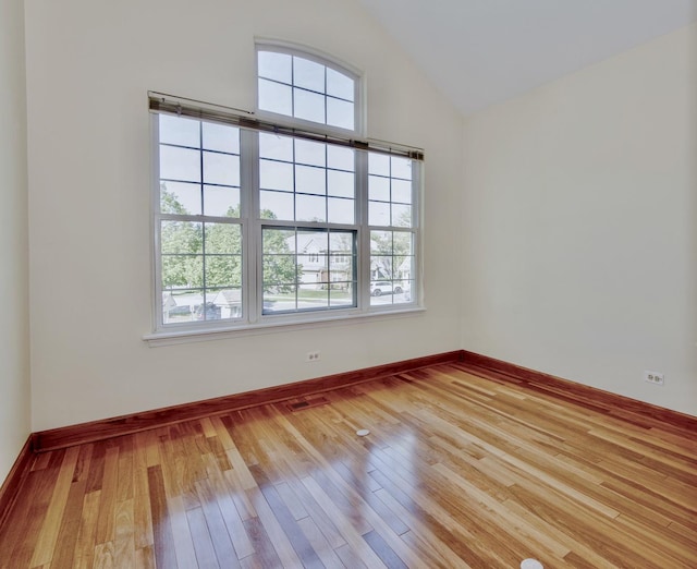 empty room featuring healthy amount of natural light, hardwood / wood-style flooring, vaulted ceiling, and baseboards