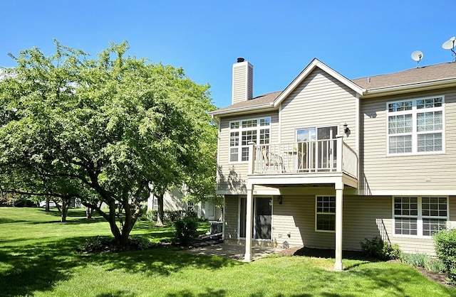 rear view of property with a balcony, a lawn, a chimney, and a patio