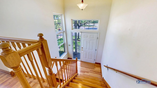 stairs featuring wood finished floors, plenty of natural light, a high ceiling, and baseboards
