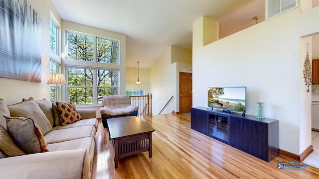 living area featuring light wood-style flooring, a towering ceiling, and baseboards