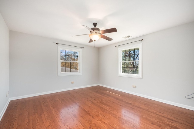 empty room featuring baseboards, visible vents, wood finished floors, and plenty of natural light