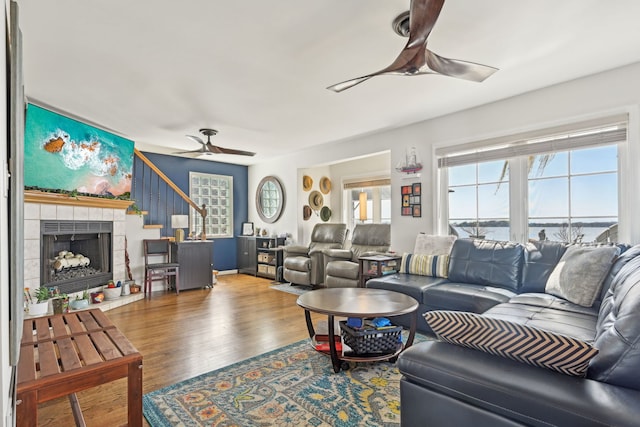 living area featuring wood finished floors, ceiling fan, a tile fireplace, and stairs