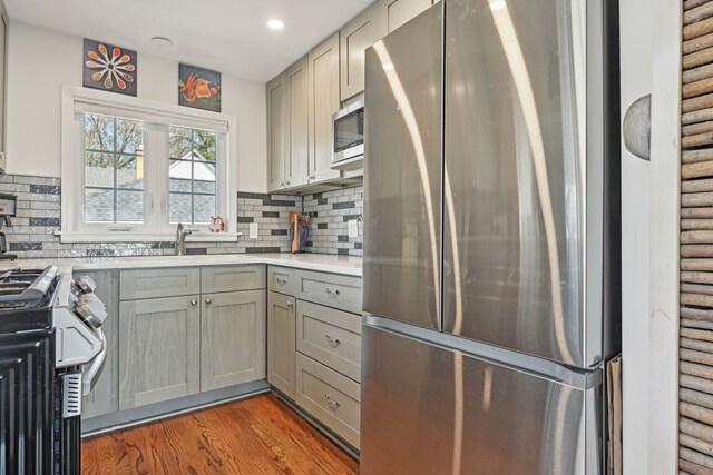 kitchen with rustic walls, decorative backsplash, stainless steel appliances, light countertops, and wood finished floors