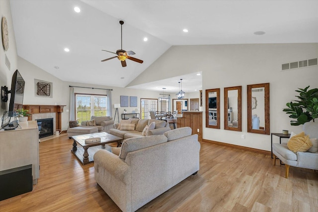 living room featuring light wood finished floors, visible vents, a fireplace, high vaulted ceiling, and ceiling fan