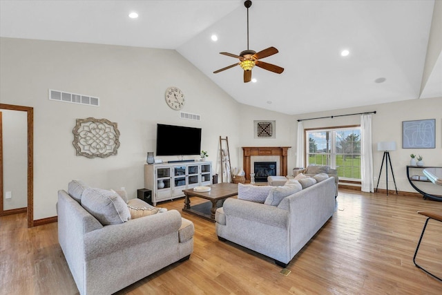 living area featuring a glass covered fireplace, visible vents, high vaulted ceiling, and ceiling fan