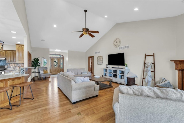 living area featuring a ceiling fan, visible vents, high vaulted ceiling, and light wood-style flooring